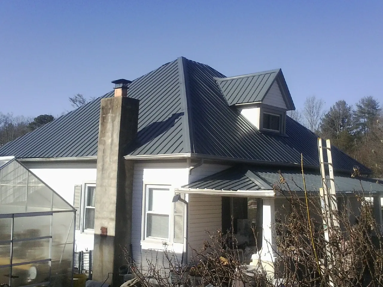 Dark blue standing seam metal roof on a white farmhouse with dormer — Slate & Tile Roof Repair by Roofing Brothers in Kemp