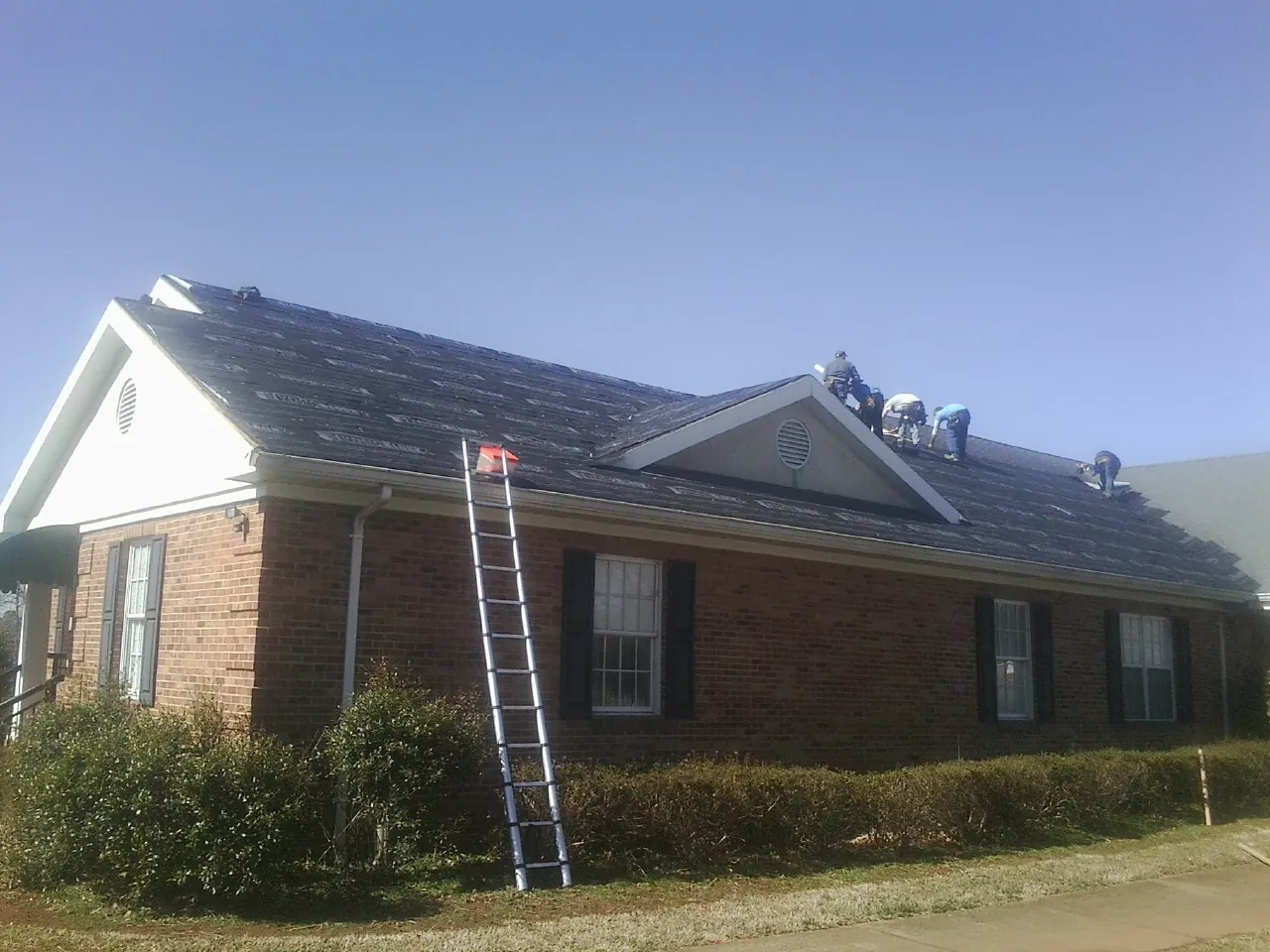 Crew tearing shingles off a brick ranch roof with a ladder set — Emergency Roof Repair work by our crew in Kemp
