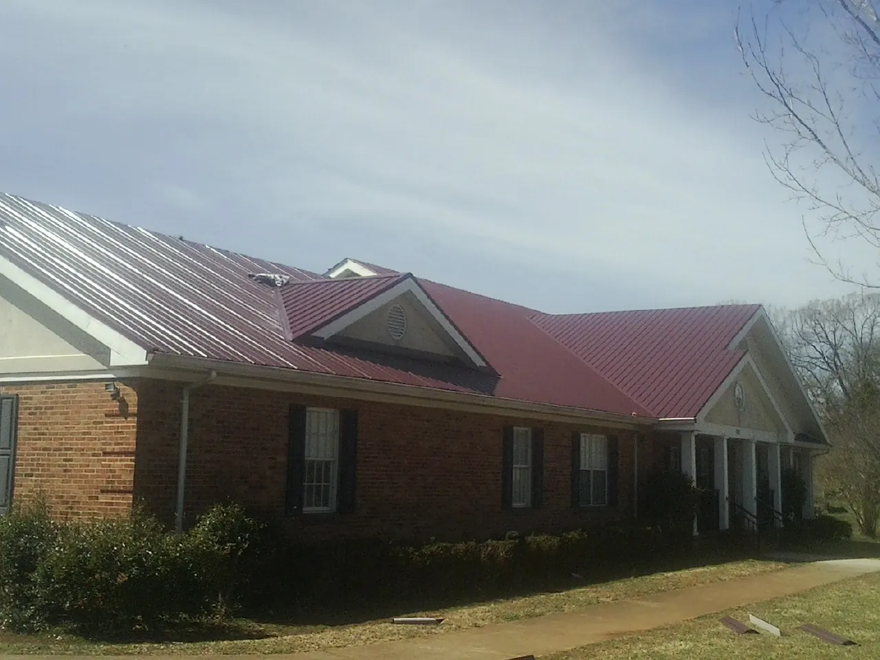 Red metal roof with gabled entries on a long brick building, from a Hail Damage Roof Repair job in Kemp