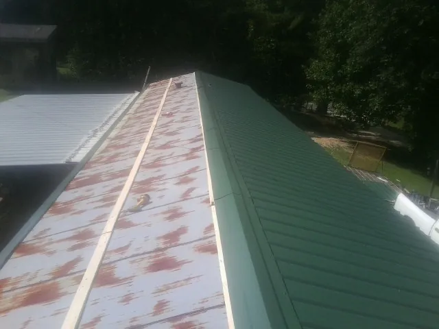 Old rusted panels beside newly installed green metal roofing — Wind Damage Roof Repair by Roofing Brothers in Kemp